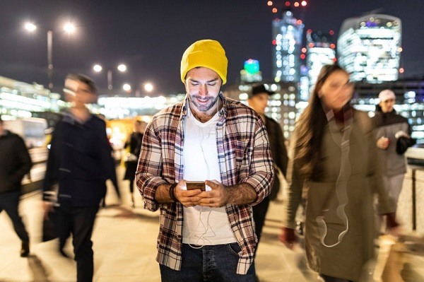 smiling man looking at his phone by night live chatting with ladies